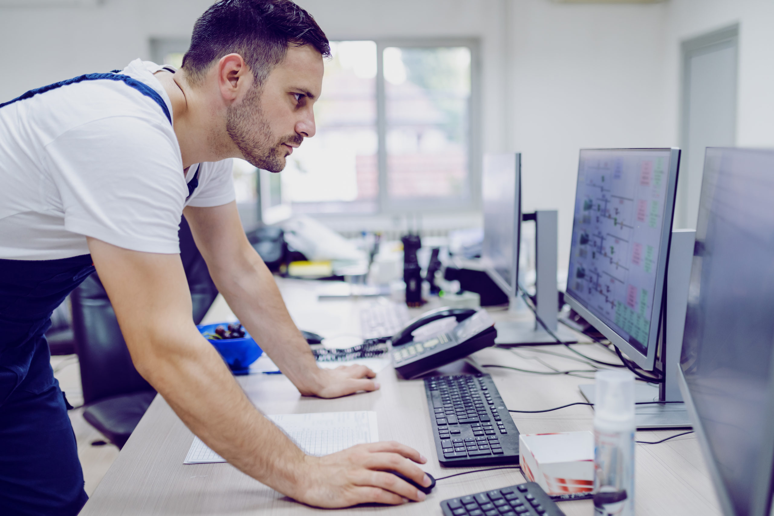Side view of serious caucasian plant worker using computer in control room. Side view of serious caucasian plant worker using computer in control room.